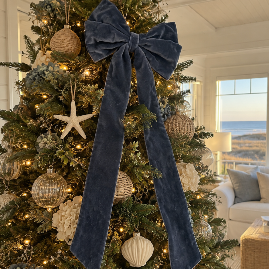  Navy velvet Christmas bow styled on an illuminated Christmas tree in an elegant coastal living room.