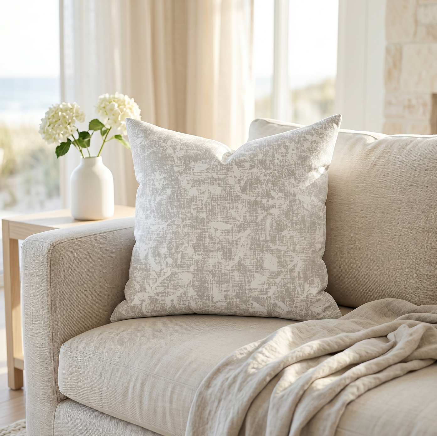 neutral abstract pattern throw pillow on a cream coastal sofa in a bright living room with ocean view
