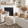 Round upholstered pouf with a muted botanical leaf print in sage, taupe, blush, and warm neutral tones.