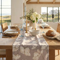 Neutral floral table runner on a light wood farmhouse dining table in a coastal home.