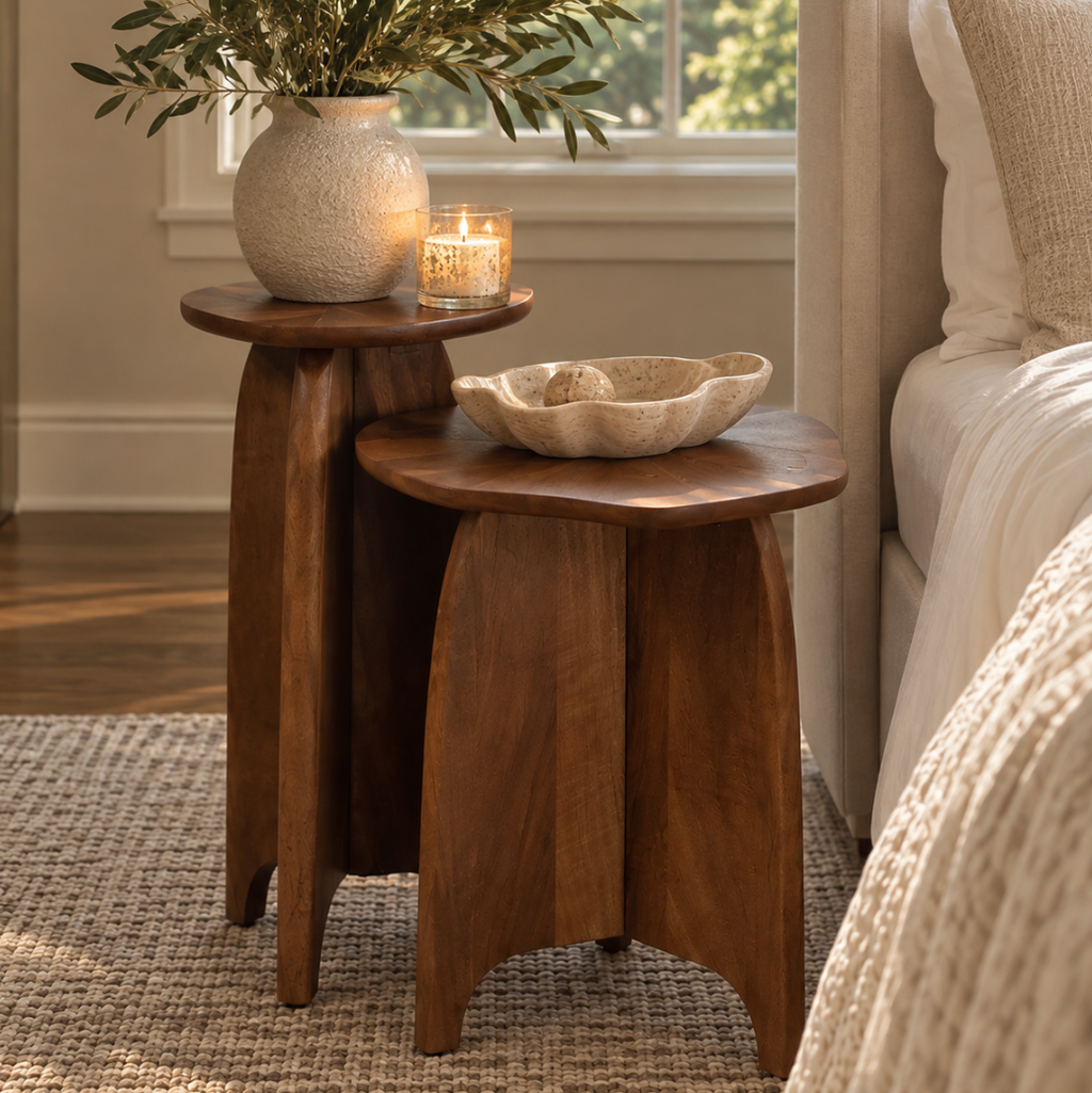 Sculptural wooden nesting side tables decorated with a ceramic bowl and vase for an understated luxury interior.