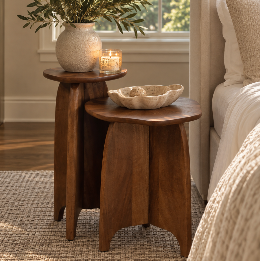Sculptural wooden nesting side tables decorated with a ceramic bowl and vase for an understated luxury interior.