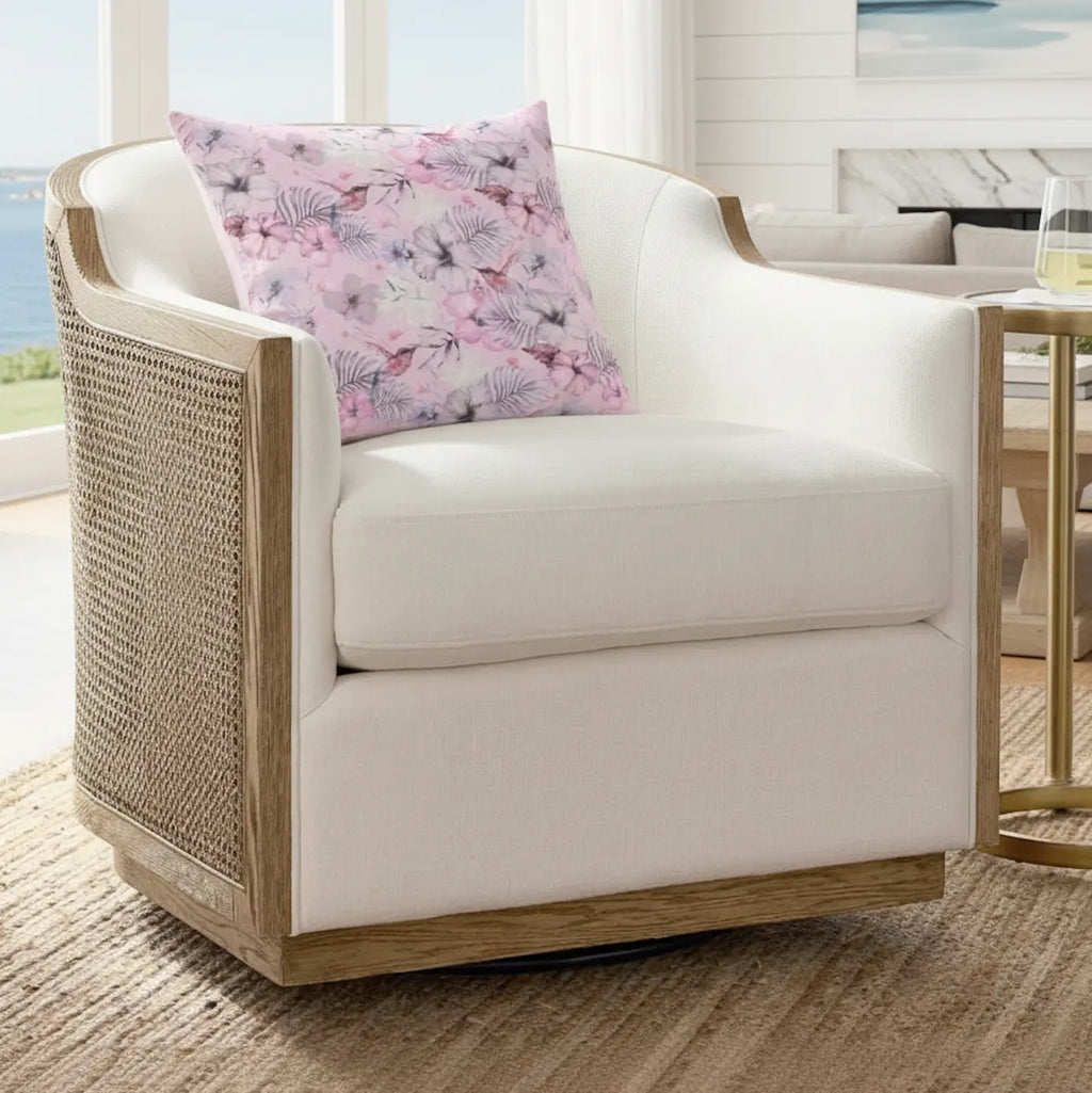 Pink floral throw pillow on a cream upholstered chair with woven rattan sides.