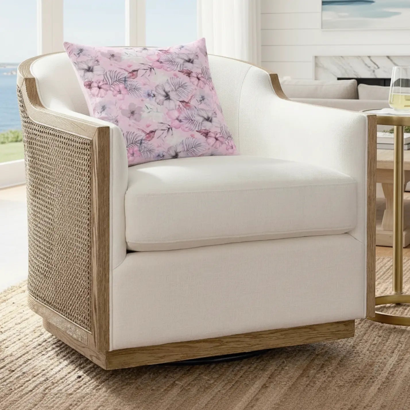 Pink floral throw pillow on a cream upholstered chair with woven rattan sides.