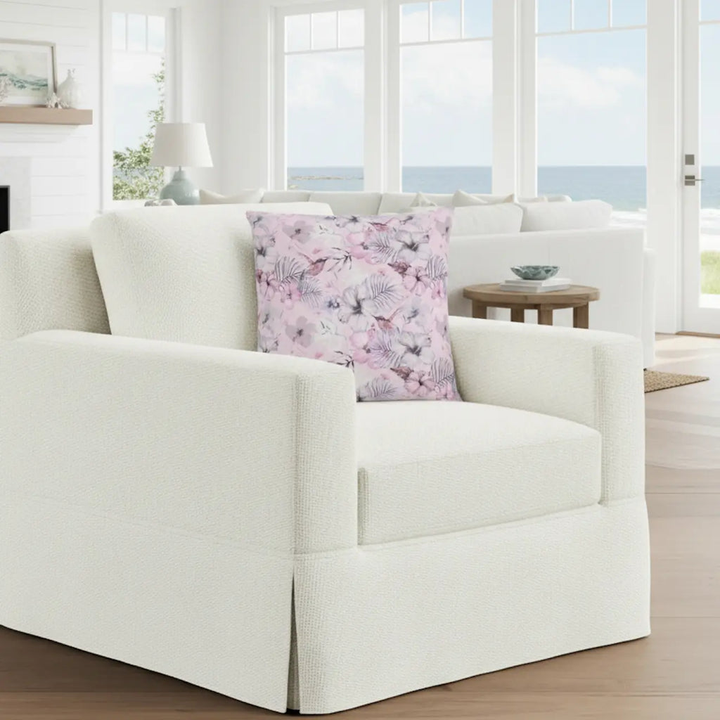 Pink floral throw pillow on a white textured sofa in a bright coastal living room.