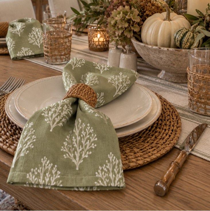 Set of 4 sage green linen napkins with white coral branch print, folded in woven rattan napkin rings for a fall table setting