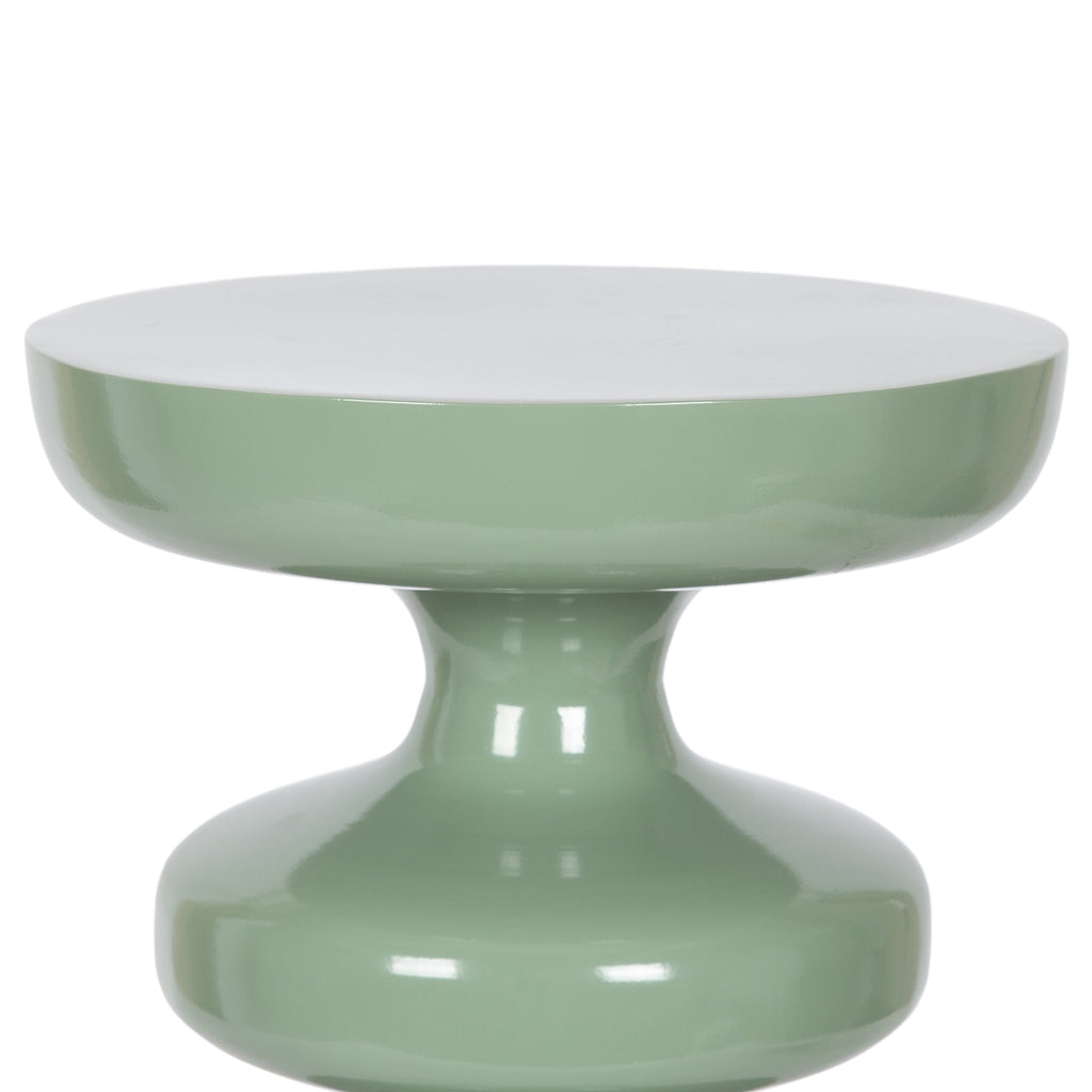 Sculptural sage green end table with a glossy finish, placed beside neutral seating and ocean‑inspired decor.