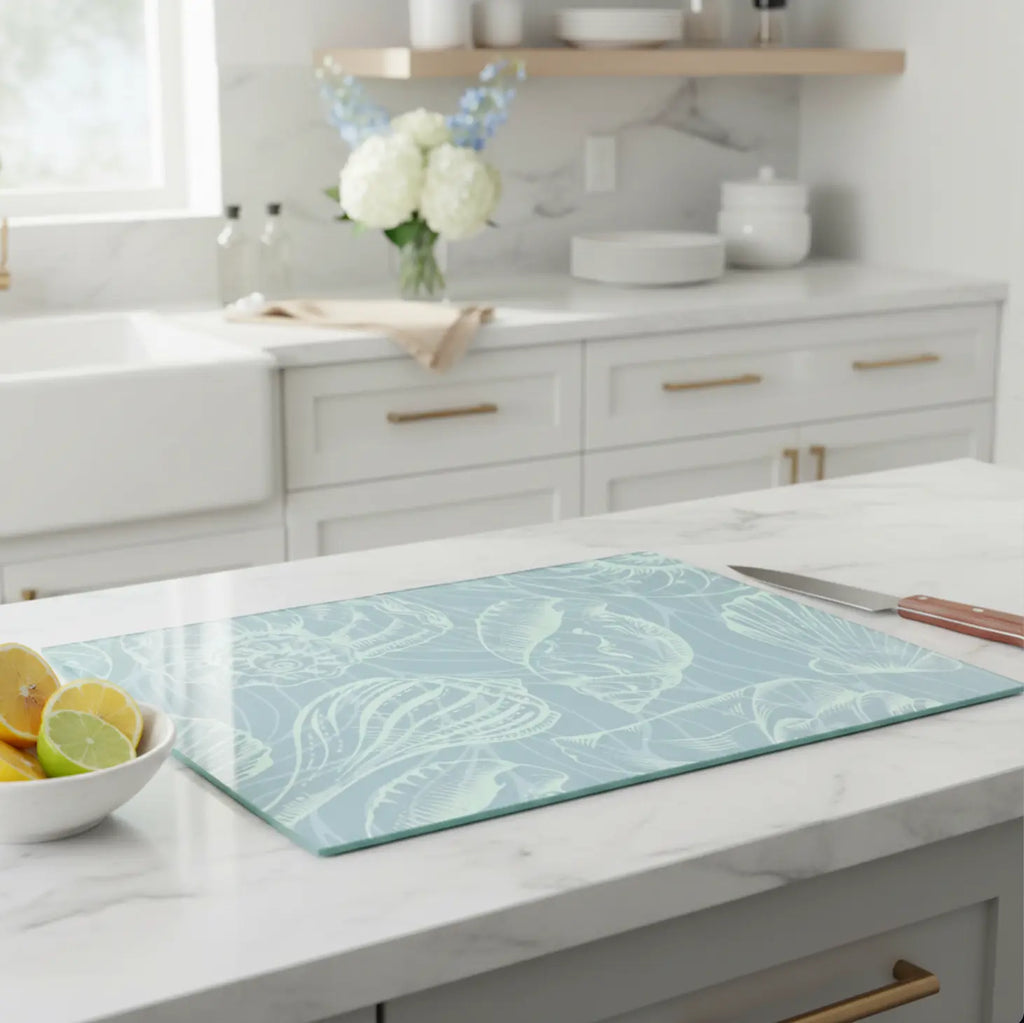Coastal seashell tempered glass cutting board in seafoam blue on a marble kitchen island with lemon bowl and knife