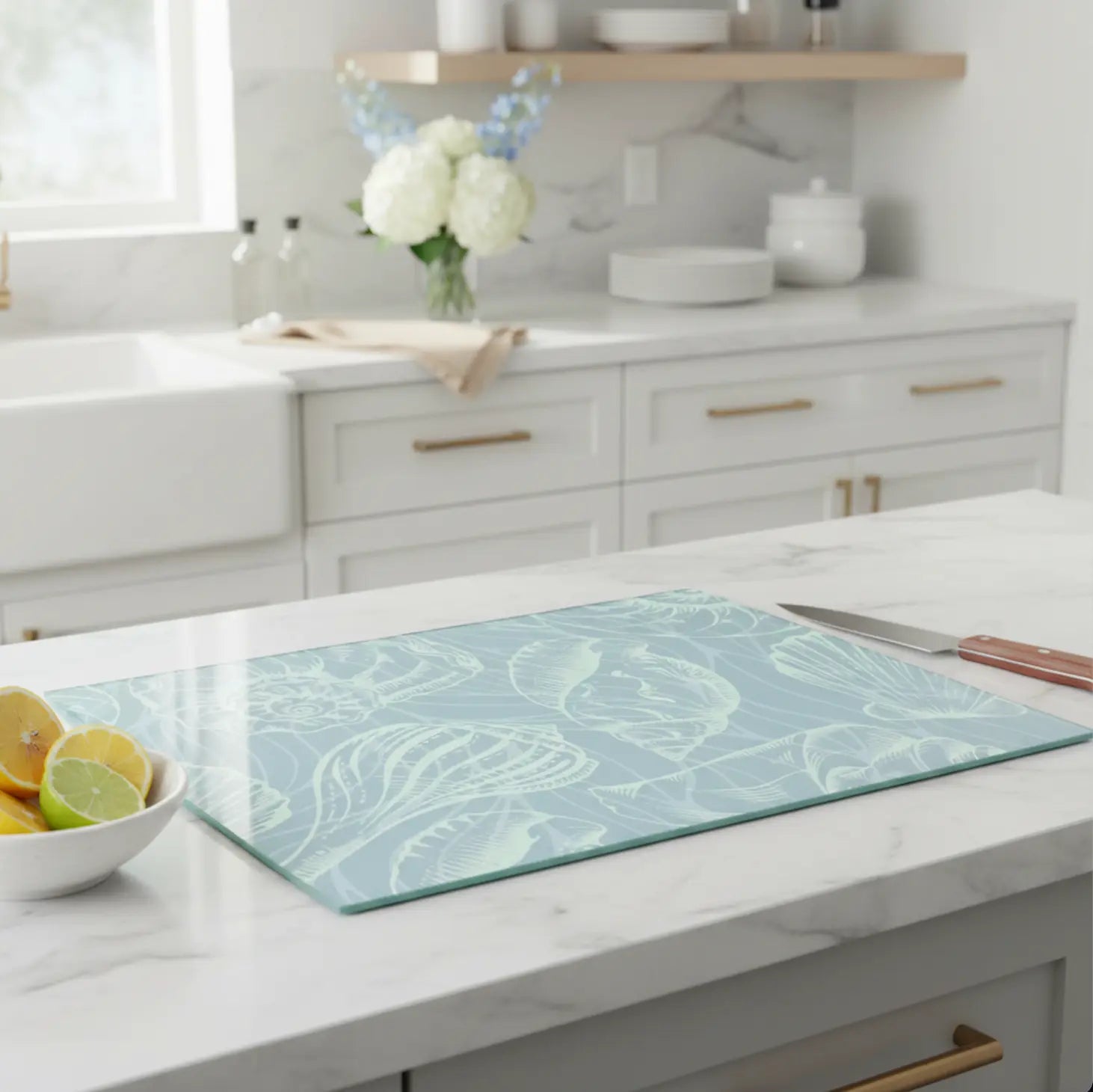 Coastal seashell tempered glass cutting board in seafoam blue on a marble kitchen island with lemon bowl and knife