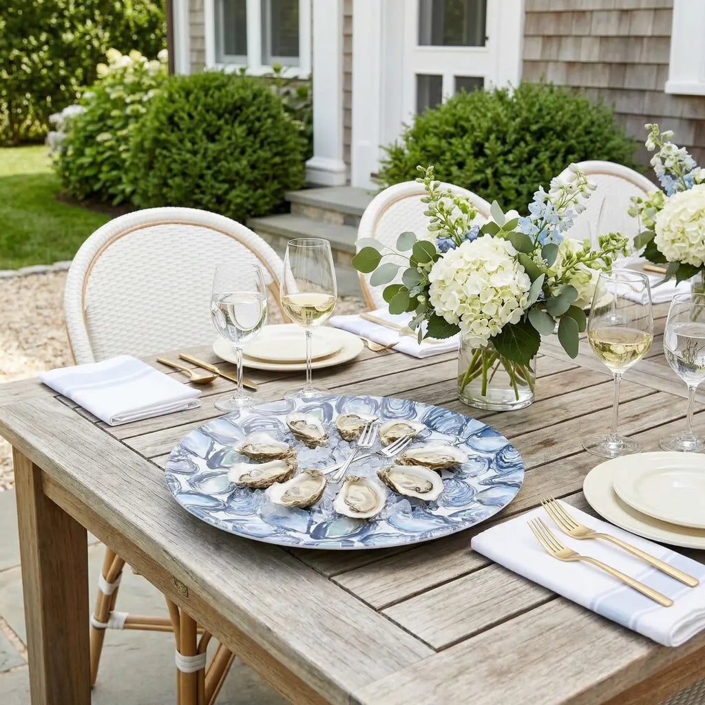 Oyster serving tray on a blue marbled plate with oysters, set on a wooden outdoor table with florals.