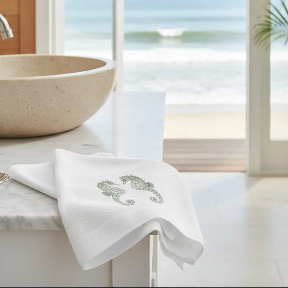 Mint Seahorse Face Towel with two mint seahorses embroidered on white towel, draped over marble counter.