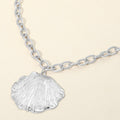 Delicate textured seashell pendant necklace worn with a simple white top for a coastal look.