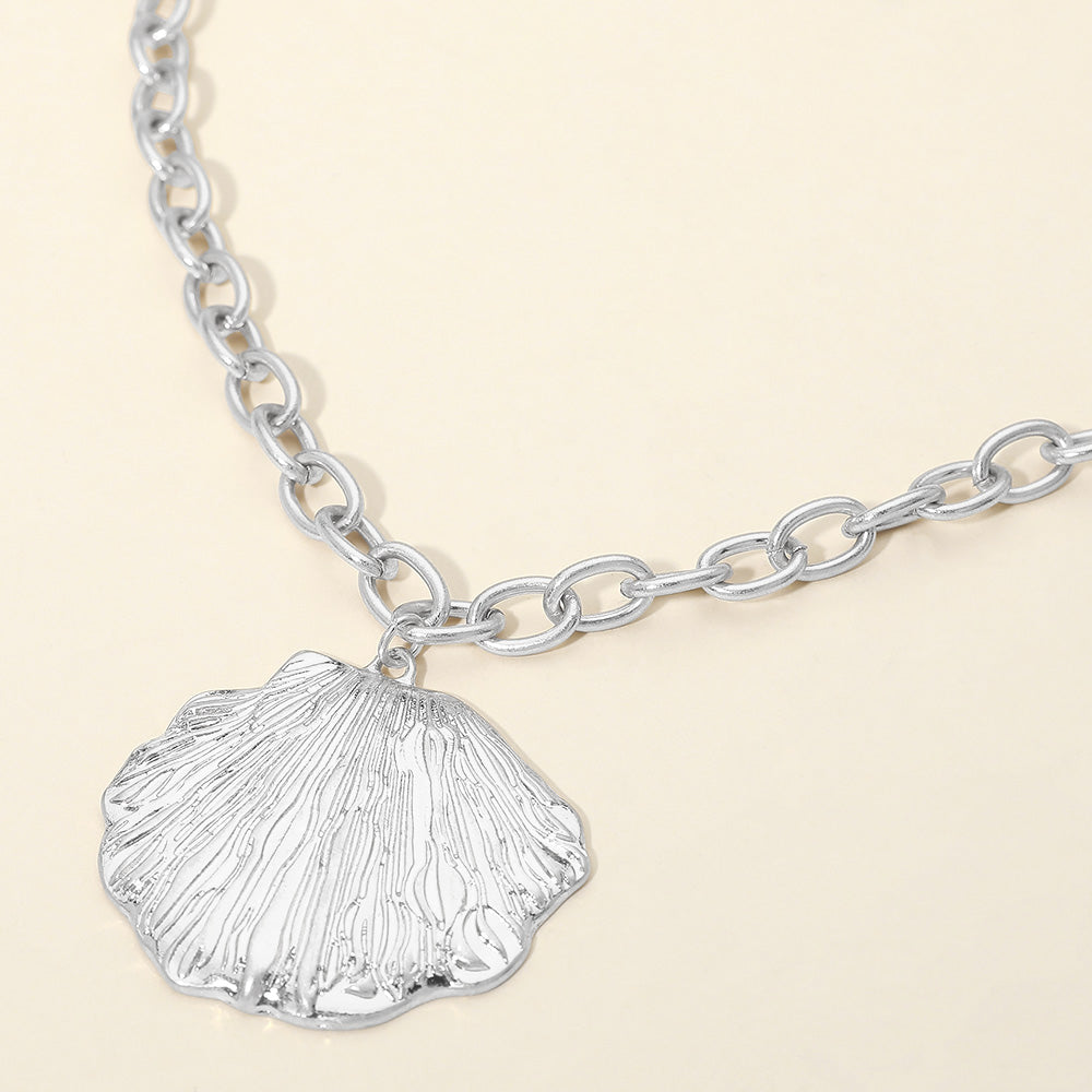 Delicate textured seashell pendant necklace worn with a simple white top for a coastal look.