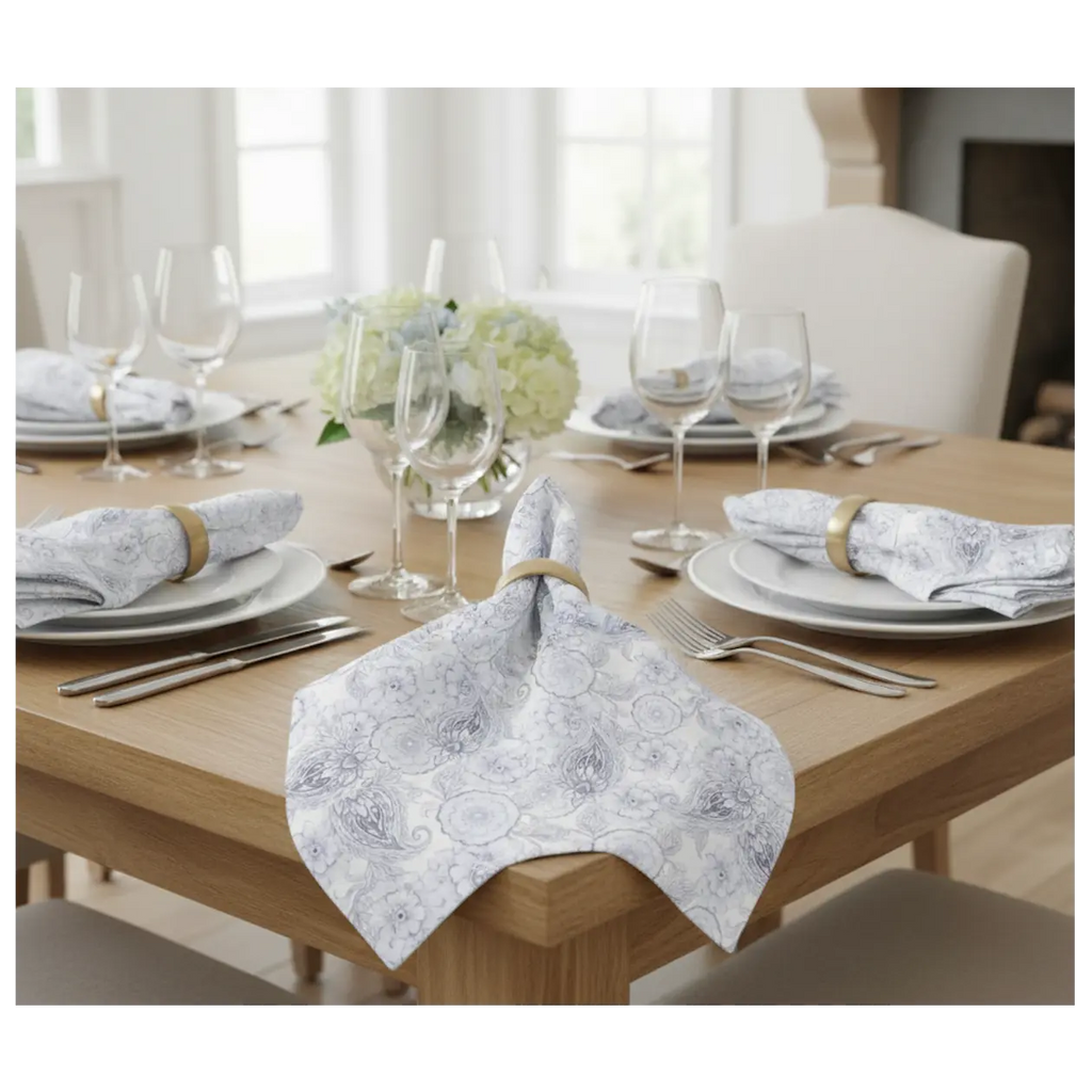 Blue paisley floral cloth napkins, set of four, folded with rings on a wooden table beside glassware.