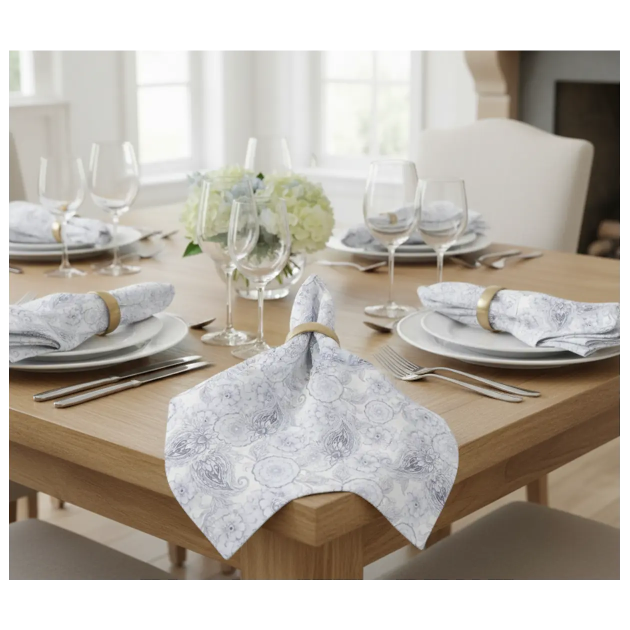 Blue paisley floral cloth napkins, set of four, folded with rings on a wooden table beside glassware.