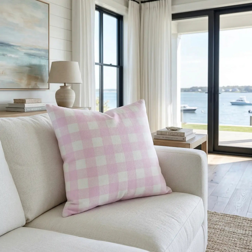 Lila Throw Pillow with pink gingham checks on a light sofa by a seaside window.