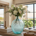 Tall light blue glass vase used as a centerpiece on a dining table.