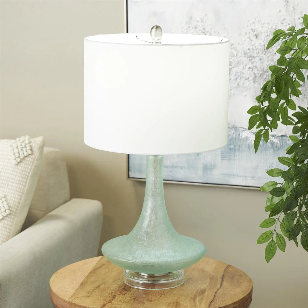 Seaglass Glow Lamp with teal seaglass base and white fabric shade on a round wood table.