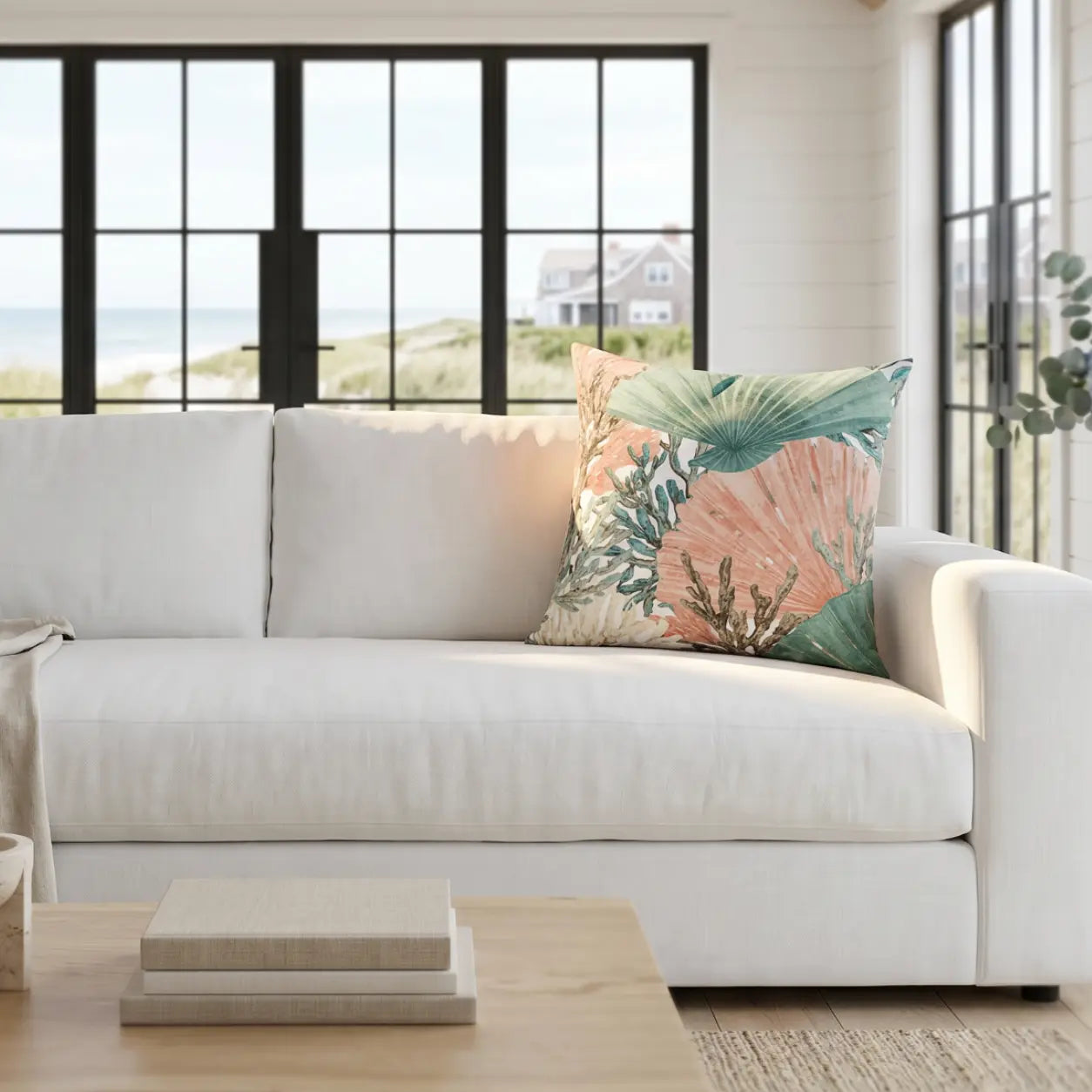 Teal and salmon coral and shell throw pillow on a neutral sofa in a coastal living room.