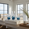 Tall wavy blue and clear glass vase with flowers styled in a beach house living room