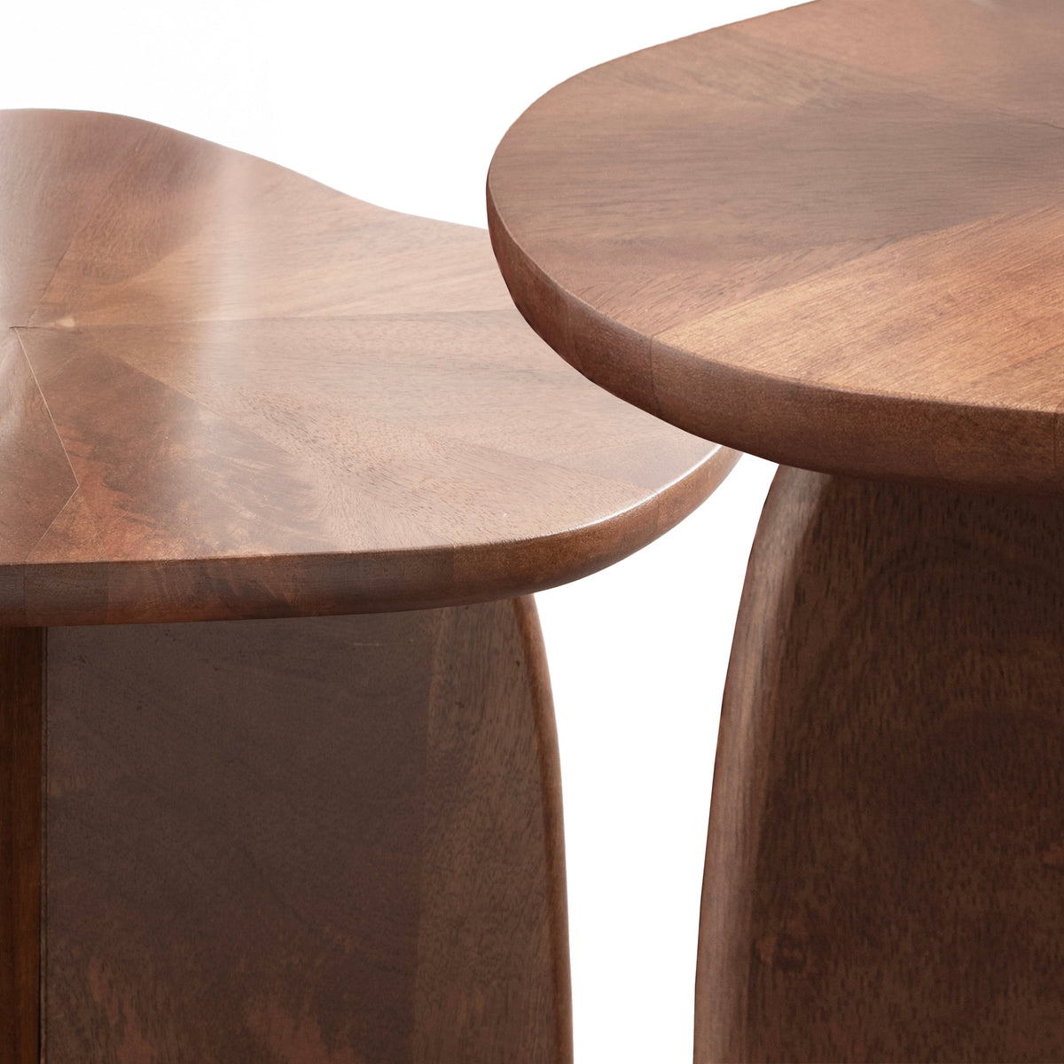 Organic modern wooden nesting bedside tables styled beside a neutral upholstered bed with natural textures.